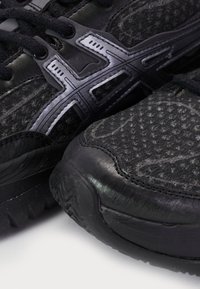 Black athletic shoes feature a textured fabric upper, sleek synthetic accents, and a rugged rubber outsole with a multi-directional tread pattern.