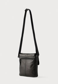 Μαύρη δερμάτινη τσάντα χιαστί με μακρύ λουρί, που διαθέτει μπροστινή τσέπη με φερμουάρ και λεία υφή, μινιμαλιστικός σχεδιασμός με ραφές.