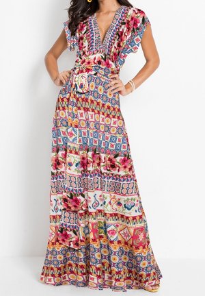 Femme portant une robe maxi bohème colorée avec des motifs floraux et géométriques, un profond décolleté en V, des manches flottantes et une ceinture nouée à la taille.