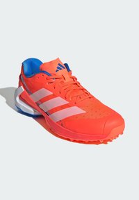 Bright red athletic shoe with a mesh upper, contrasting blue accents and three white stripes, featuring a textured sole with spikes for grip.