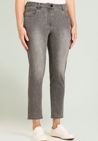 Pantalon en denim gris à coupe droite, avec des accents en strass, cinq poches et une fermeture par bouton. Porté avec des baskets blanches.