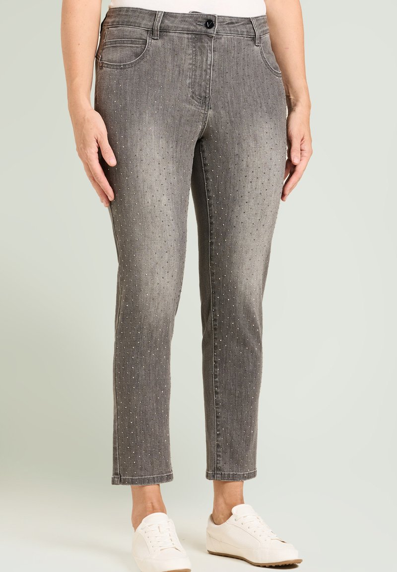 Pantalon en denim gris à coupe droite, avec des accents en strass, cinq poches et une fermeture par bouton. Porté avec des baskets blanches.