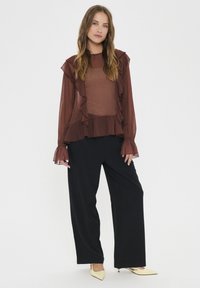 Brown sheer blouse with ruffles at the neckline and cuffs, paired with black wide-leg trousers and yellow pointed-toe heels.