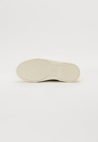 Hvit gummisåle med teksturert overflate, med pregete merke- og design detaljer, rund form og glatte kanter.
