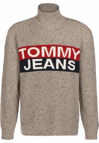 Pull beige avec une texture côtelée, un col haut et un motif à rayures audacieuses comportant "TOMMY" en rouge et "JEANS" en blanc et bleu marine.