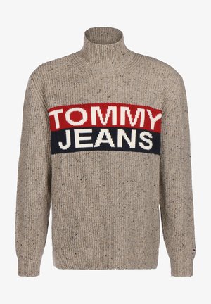 Pull beige avec une texture côtelée, un col haut et un motif à rayures audacieuses comportant "TOMMY" en rouge et "JEANS" en blanc et bleu marine.