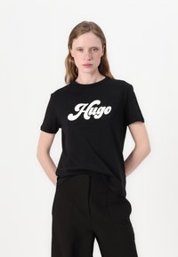 Černé tričko s výrazným bílým logem "Hugo". Krátké rukávy, kulatý výstřih, vyrobeno z měkké bavlny. V kombinaci s černými kalhotami.