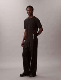 Črni bombažni T-maica s kratkimi rokavi in ožjim krojem, ki vsebuje subtilen logotip Calvin Klein. Ustrezajo ji ohlapne črne hlače in črne čevlje.