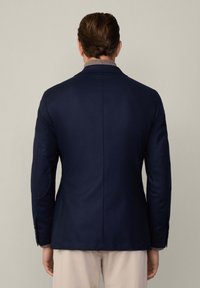 Blazer blu navy con una texture liscia, revers a punta e toppe sui gomiti. Presenta un taglio sartoriale e polsini con bottoni.