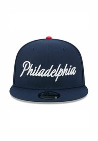 Casquette snapback bleu marine avec une broderie blanche en cursive "Philadelphia" à l'avant, un bouton rouge sur le dessus et une visière plate.