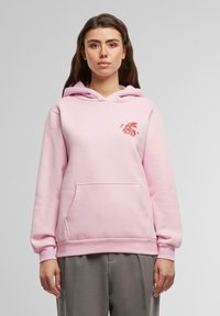 Sudadera rosa claro con un bolsillo frontal, capucha con cordón y un gráfico rojo de un conejo y el número 88 en el pecho. Textura de tela suave.