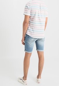 Camisa de manga corta a rayas en blanco, rosa y azul, combinada con shorts de mezclilla azul claro y zapatillas blancas. Atuendo casual de verano.
