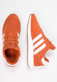 Oranga sneakers i textil och mocka, med vit tre-stripes branding, en vadderad krage och en dämpad vit mellansula.