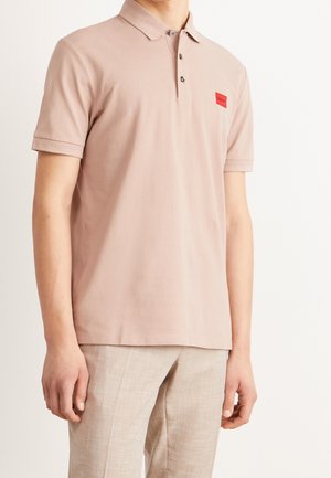 Ljusrosa pikétröja i bomull, med knäppning i två knappar, ribbad krage och en liten röd logopatch på bröstet.