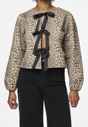 Lange mouw top met luipaardprint en drie grote zwarte lintstrikken aan de voorkant, gecombineerd met een zwarte broek met hoge taille.