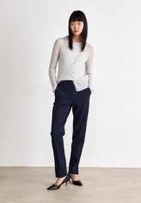 Cardigan grigio chiaro leggero e trasparente a coste, con lunghe maniche e bottoni, abbinato a pantaloni blu navy su misura e décolleté nere a punta.