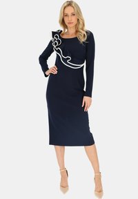 Granatowa sukienka z długim rękawem, z falbaną w kolorze białym, dopasowany fason i długość do kolan. Gładka tekstura materiału z delikatnym rozciągnięciem.
