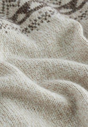 Stickad tyg i beige med ljusbruna prickar, med ett subtilt geometriskt mönster. Mjuk textur med veck och draperad look.