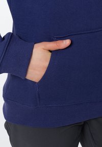 Granatowy sweter z kangurzą kieszenią, ściągaczami przy mankietach i u dołu. Miękka faktura z widocznymi szwami wzdłuż brzegów.