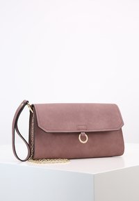 Torba z faux zamszu w kolorze delikatnego różu, z klapką, złotymi elementami i odpinanym łańcuszkiem. Posiada okrągły akcent z przodu.