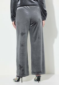 Graue Samt-Hosen mit weitem Bein und glatter Textur, mit einem hohen Bund und leichtem Glanz. Kombiniert mit bunten Sandalen mit Riemchen.
