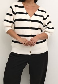 Neulejakku, jossa mustavalkoiset raidat, syvä V-aukko, ylisuurennetut hihat ja napitus. Pehmeä pinta ja rento istuvuus.