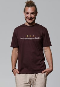 T-shirt à manches courtes bordeaux en coton, orné d'images et de texte décoratifs dans une couleur contrastante sur le devant.