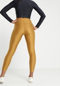 Leggings a vita alta di colore giallo senape realizzati in materiale elasticizzato, con una texture liscia e un logo Nike nero sul retro.