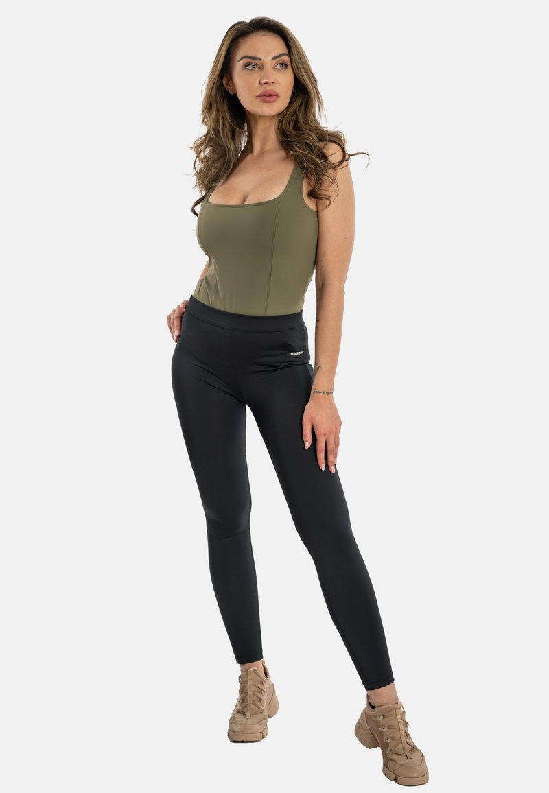 Vihreä oliivi bodysuit, jossa on syvä kaula-aukko, yhdistettynä korkeavyötäröisiin mustiin legginsseihin. Ruskeat nauhakengät täydentävät asun.