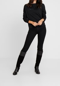 Sweat-shirt noir à col rond, associé à un jean skinny noir et des bottes noirs hautes jusqu'aux genoux, avec une bande brillante en haut.