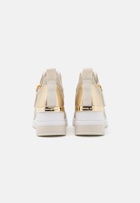 Sneaker con una combinazione di morbido suede beige e accenti metallici dorati, con una suola in gomma bianca e dettaglio del tallone con marchio.
