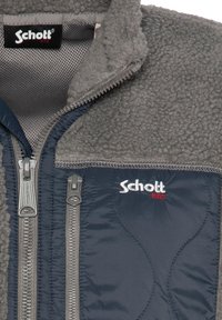 Giacca in pile con corpo grigio, sezioni blu navy e zip argentate. Presenta tasche laterali e un logo ricamato in bianco e rosso.