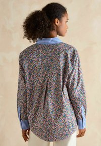 Floral-patterned shirt in multicolored fabric with a blue and white striped collar and cuffs. Relaxed fit with long sleeves and button details.