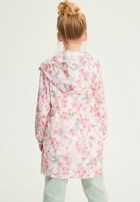 Imperméable à motif floral avec une base rose, doté d'une capuche, de poignets élastiques et d'une taille cintrée. Tissu léger avec une texture lisse.