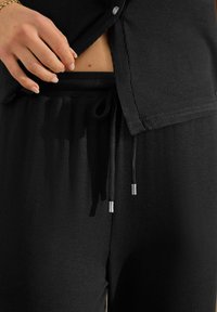 Ensemble de loungewear noir en côte, comprenant un haut à boutons et un pantalon à cordon de serrage, avec des accents en métal argenté et une texture douce.