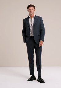 Costume bien ajusté bleu marine en tissu texturé, comprenant un blazer à un bouton, un pantalon slim et des chaussures de ville noires brillantes.