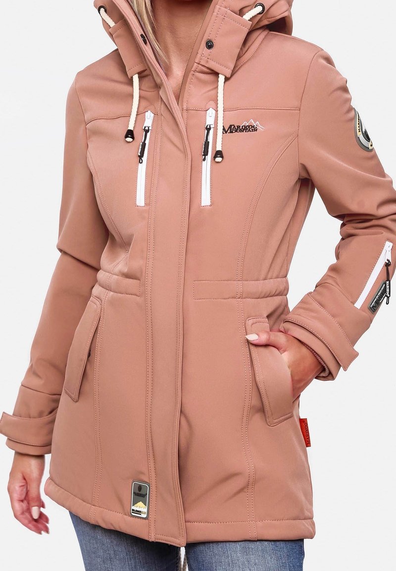 Veste d'extérieur rose douce avec capuche, poches zippées blanches sur la poitrine et la manche, main dans la poche latérale, portée avec un jean bleu.