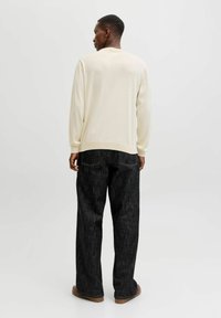 Maglione leggero color crema con polsini e orlo a costine, abbinato a jeans in denim scuri. I jeans hanno una vestibilità comoda e tasche posteriori minime.