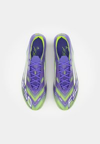 Purple and green soccer cleats with a textured upper, featuring a zigzag pattern and white F50 branding, secured by purple laces.