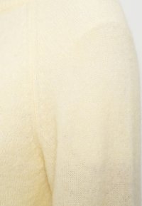 Ανοιχτό κίτρινο πουλόβερ με απαλότητα και αφράτη υφή. Διαθέτει απλό σχέδιο με στρογγυλεμένο λαιμό και ριμπ λεπτομέρειες κατά μήκος των ραφών.