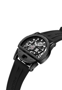 Czarny zegarek na rękę z prostokątną kopertą, przezroczystym tarczem, gumowym paskiem oraz skomplikowanym wzorem z przekładniami, z srebrnymi akcentami i czerwoną detalem.