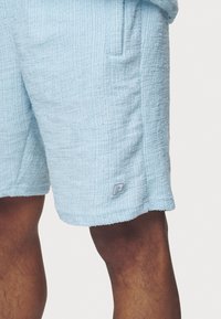 Shorts bleu clair en tissu texturé avec un motif côtelé, dotés de poches latérales et d'un petit patch logo sur l'ourlet.