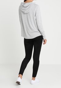 Haut en coton gris avec capuche, manches raglan et coupe décontractée, associé à des leggings noirs et des baskets blanches, vu de dos.