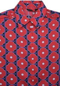 Rotes Hemd mit Blumenmuster, das große rote Blumen mit weißen Mittelpunkten und grünen Blättern auf einem marineblauen Hintergrund zeigt.
