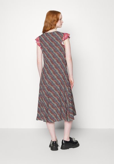 Vestido preto com um padrão ondulado em vermelho, branco e azul, apresentando mangas curtas com babados. Usado com sapatos de plataforma pretos.