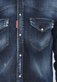 Tamsiai mėlyna džinsinė marškiniai su išblukusiomis vietomis, su perlų spaudimo mygtukais ir dviem krūtinės kišenėmis. Raudona etiketė kairėje pusėje.