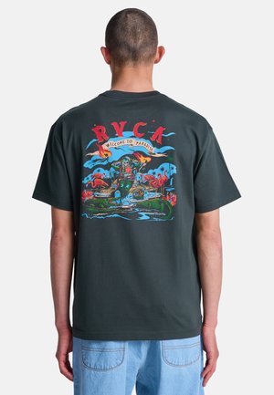 Osoba ubrana w ciemny t-shirt z kolorową grafiką szkieletu trzymającego płonące pochodnie, różowymi flamingami i aligatorem pod napisem "RVCA Welcome to Paradise".