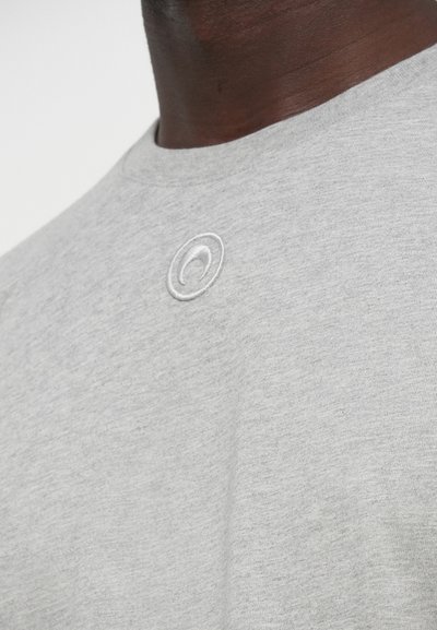 Sivé bavlnené tričko s okrúhlym výstrihom a malým bielym vyšívaným logom na hrudi. Mäkká, textúrovaná látka.