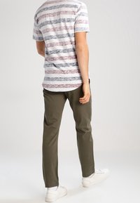 T-shirt à rayures à manches courtes en blanc, marine et bordeaux, associé à un pantalon vert olive. Ajustement décontracté avec une texture lisse et un col rond.