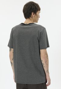 Black and gray striped short-sleeve shirt with a round neckline. Cotton material with a soft texture. Visible tattoo on the left arm.